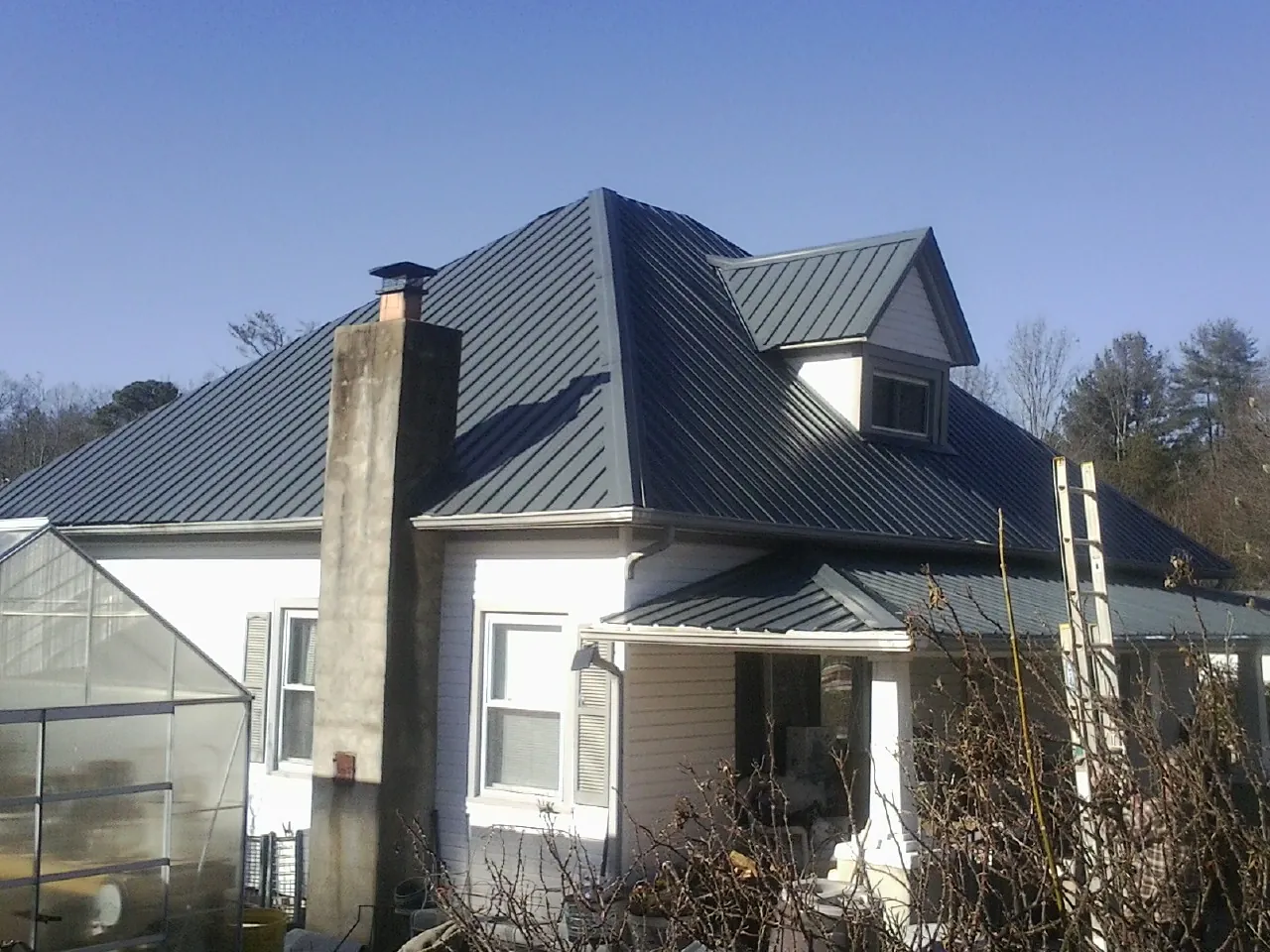 Dark blue standing seam metal roof on a white farmhouse with dormer — Slate & Tile Roof Repair by Roofing Brothers in Hooven