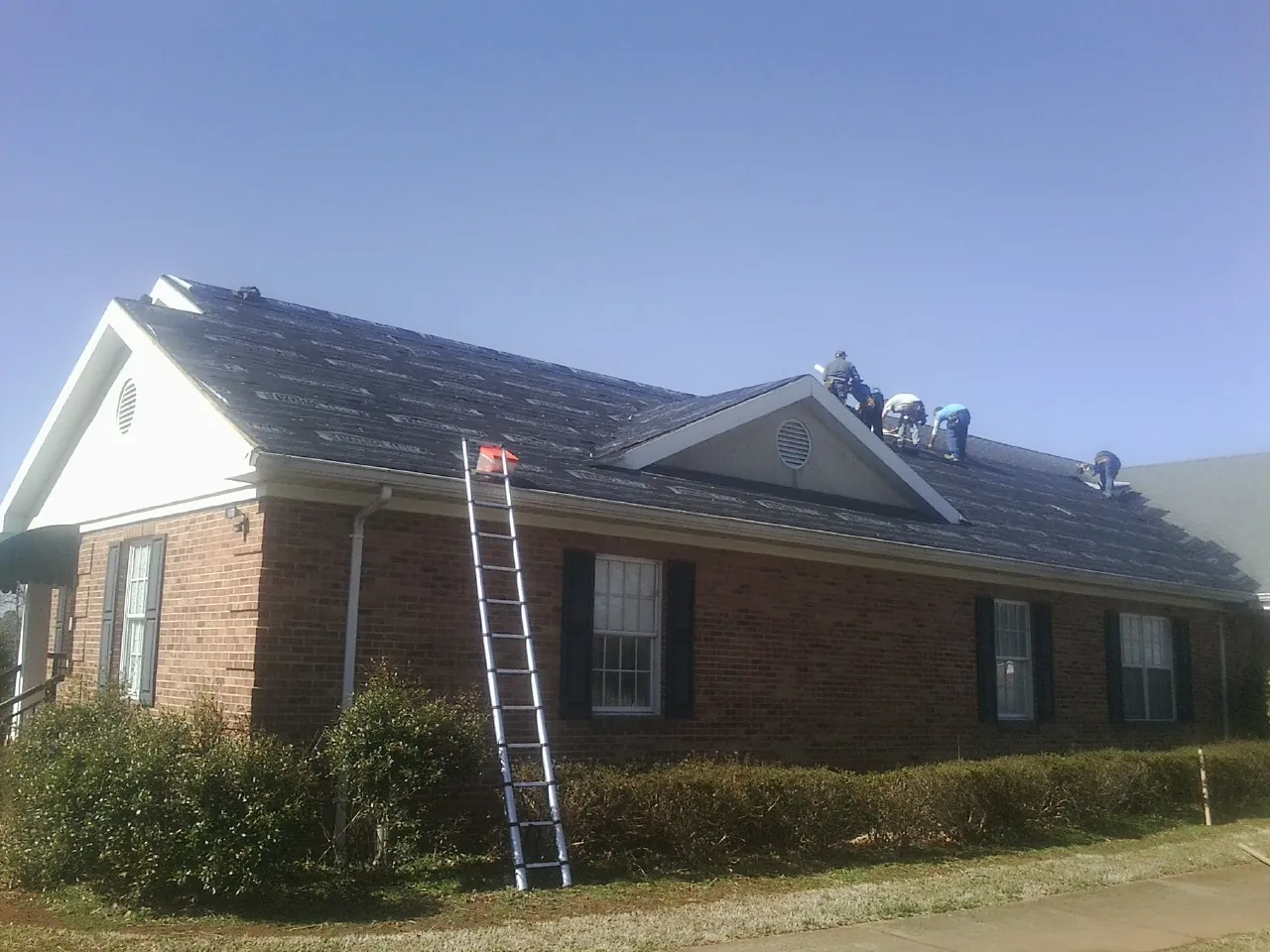 Crew tearing shingles off a brick ranch roof with a ladder set — Metal Roof Repair work by our crew in Hooven