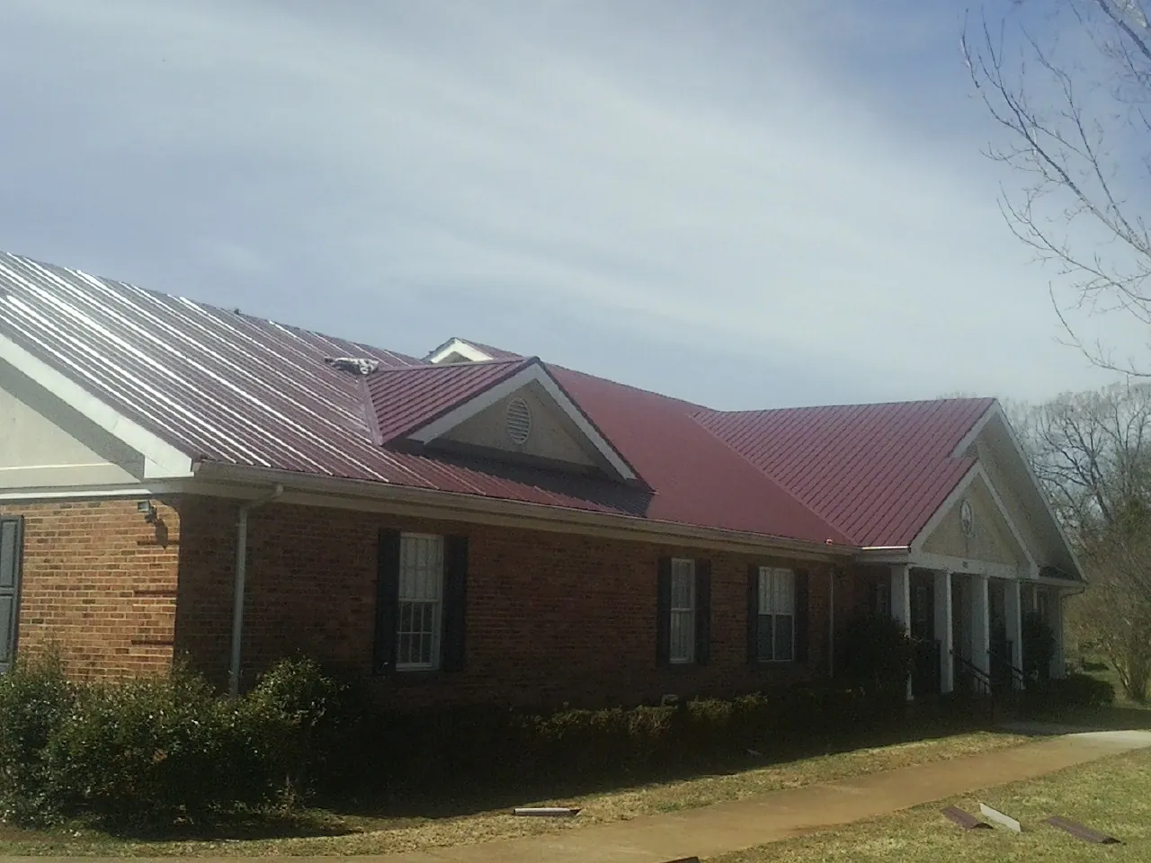 Red metal roof with gabled entries on a long brick building, from a Hail Damage Roof Repair job in Hooven
