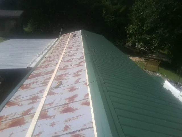 Old rusted panels beside newly installed green metal roofing — Wind Damage Roof Repair by Roofing Brothers in Hooven