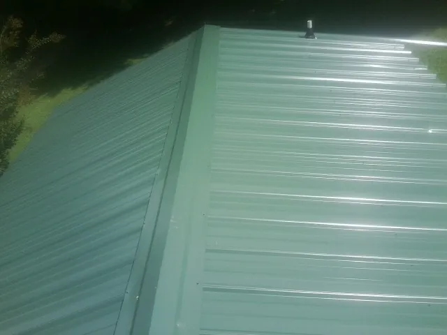 New green metal panels meeting at the ridge of a roof — Flat Roof Repair work by our crew in Hooven