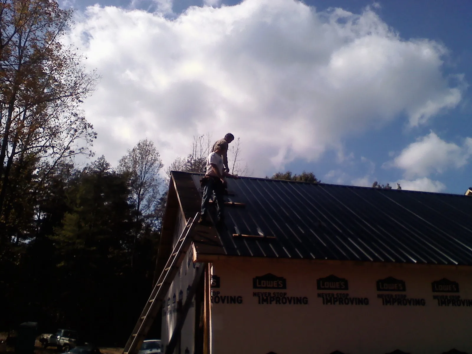 Roofer fastening dark metal panels high against a cloudy sky, from a Roof Inspection job in Hooven